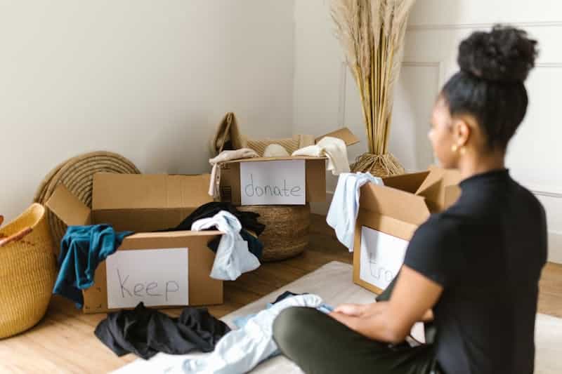 A women sitting on the floor surrounded by boxes labeled 'Keep,' 'Donate,' and 'Toss' as part of decluttering and organizing hacks