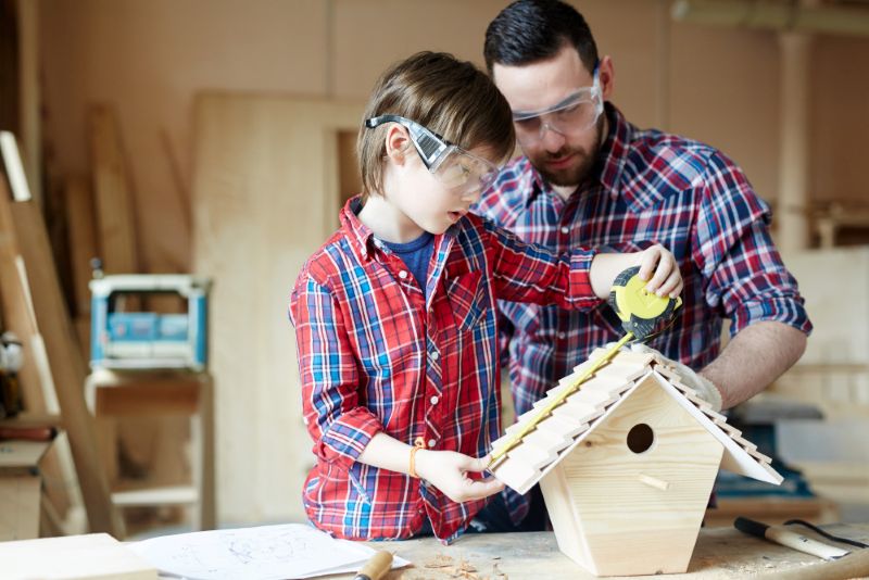 A father and son working together on building a birdhouse, using a measuring tape and safety goggles, demonstrating hands-on skills from Wutawhelp Guides for your home makeover