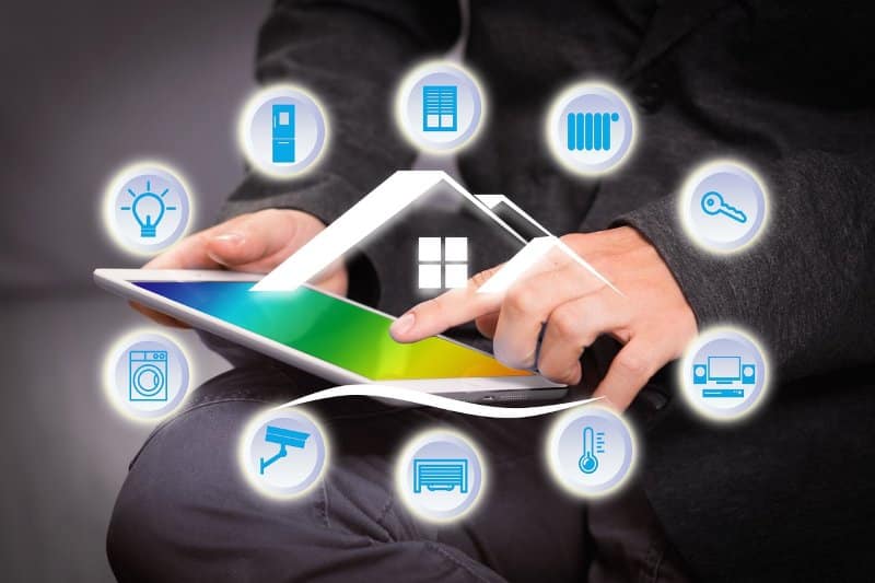A person using a tablet to control various smart home devices. Icons surrounding the tablet represent different components of a smart home, such as lighting, temperature control, security cameras, door locks, and appliances, symbolizing the interconnectedness of modern smart home technology.