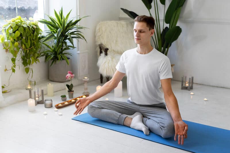 A person meditating on a yoga mat surrounded by plants and candles, creating a peaceful and calm environment for mindfulness and relaxation. TimesHealthMag.com provides insights on the benefits of mindfulness practices for overall health.
