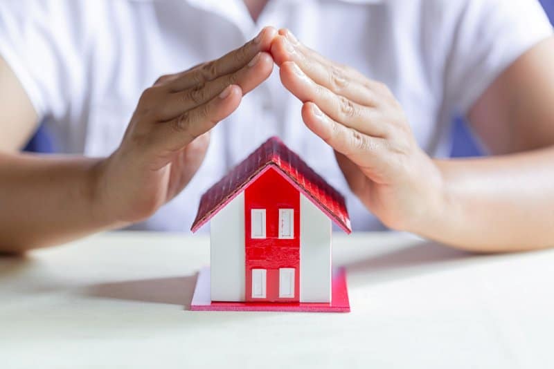 A person placing their hands above a model house, symbolizing protection and care. This could relate to the security and peace of mind homeowners receive through services like Choice Home Warranty.