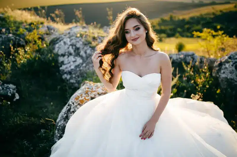 Bride in a strapless wedding dress, sitting gracefully outdoors, with soft curls in her hair, showcasing a peaceful and confident expression. Ideal for a "wedding workout plan" related visual.