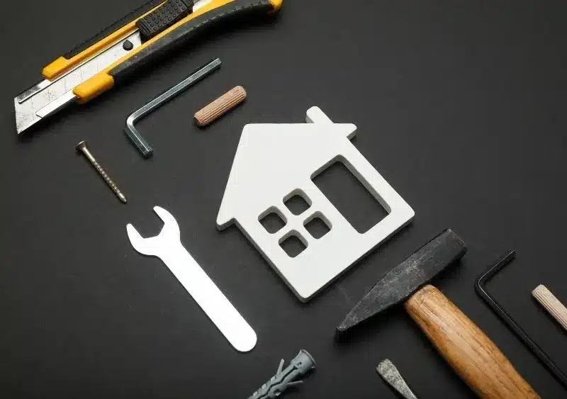 Flat lay image of property maintenance tools including a utility knife, wrench, hammer, Allen keys, screw, and a white house-shaped cutout, symbolizing property maintenance and home care in Fredericksburg.