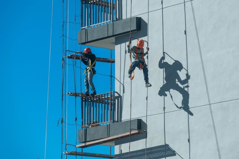 Beyond the Harness: Engineering the Future of the Fall Protection Solution Workers using engineered fall protection systems with harnesses and rope access while performing exterior building maintenance at height.