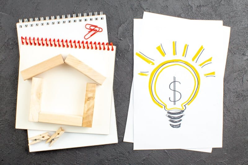 Top 5 Practical Methods to Reduce Home Utility Costs Illustration showing a house model and a light bulb with a dollar sign, representing practical methods to reduce home utility costs through energy efficiency and savings.