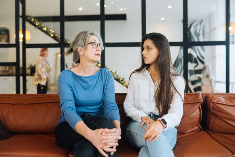 Older woman and teenage girl sitting on a sofa talking, showing parent-teen communication in Chelsea Acton Famous Parenting.
