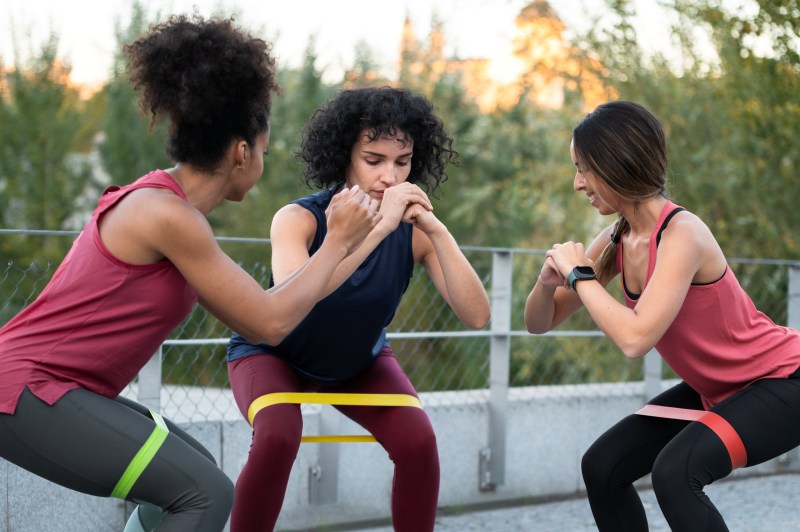 Friends doing resistance band squats together outdoors, staying active and energized, a fun option for Things to Do With Friends When Bored.