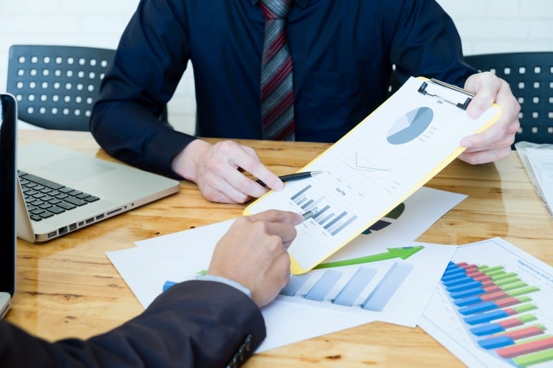 Business brokers reviewing financial charts and documents while discussing valuation and closing steps in a business sale.