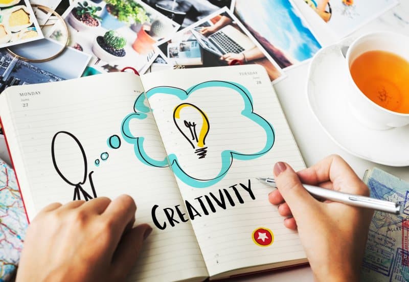Writing creative ideas in a notebook with photos and tea on desk, a simple activity showing Things to Do When Bored to spark creativity.
