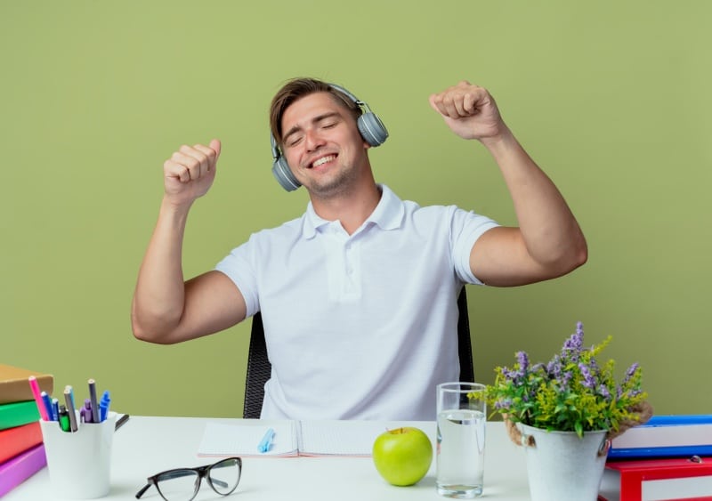 Man wearing headphones enjoying music at desk during break, simple Things to Do When Bored activity to refresh mood and relax mind.