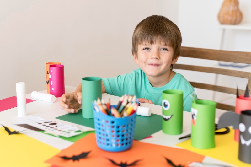 Child doing paper craft at a table with colored paper, pencils, and DIY art supplies.