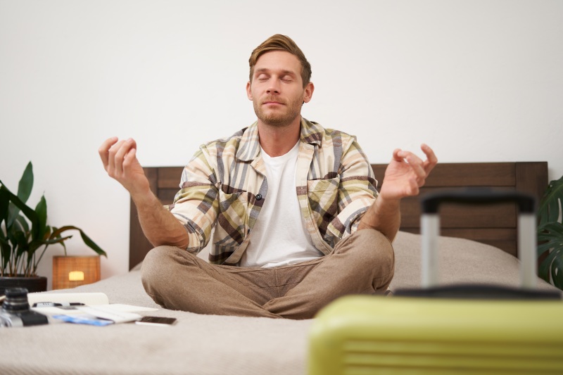 Man sitting cross-legged on a bed and meditating in a calm room.