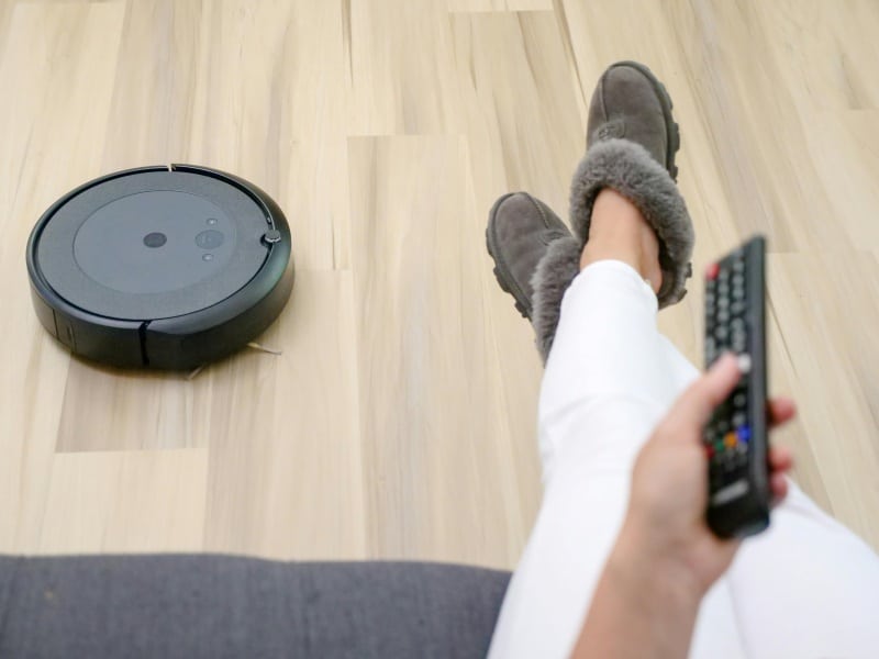 Automated Appliances robot vacuum cleaning the floor while a person controls the smart home device with a remote.