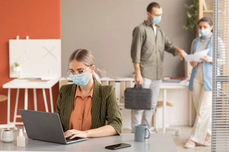 Best Practices for Maintaining a Clean and Healthy Work Environment Employees wearing masks in a clean office, showing a safe and healthy work environment with hygiene practices.
