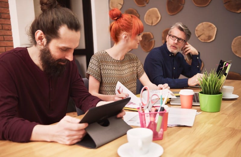 Contact TheBoringMagazine team members working at a table with tablets, notes, laptop, and office supplies.