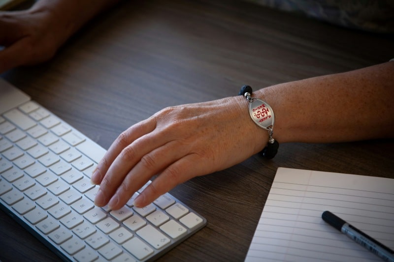 Understanding the Importance of Medical ID Jewelry: A Lifesaver in Emergencies Person wearing Medical ID Jewelry bracelet while using a keyboard, showing emergency medical alert information.