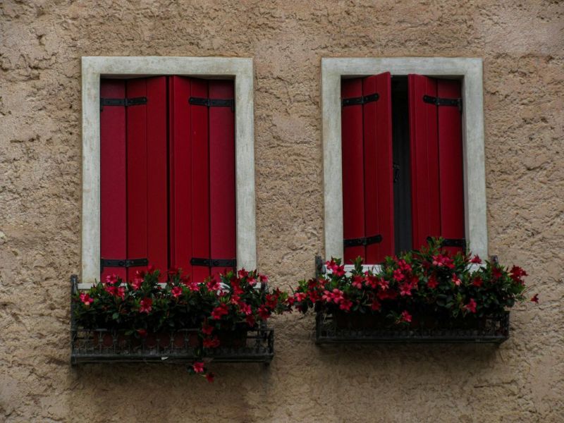 Red exterior window shutters on home windows with flower boxes, showing durable and custom window shutters design for privacy and style.