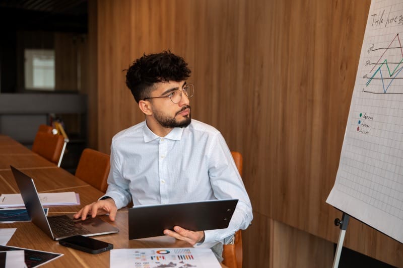 The Career-Transforming Power of an Online MBA in Business Analytics Professional reviewing business analytics data on a tablet beside a performance chart in a meeting room.