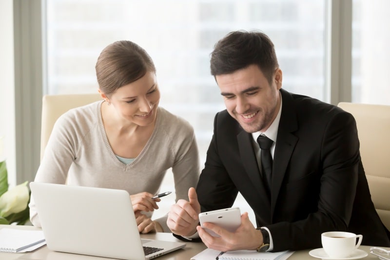 Key Benefits of Direct Deposit for Employees and Employers Two employees reviewing direct deposit payroll details on a smartphone beside a laptop.