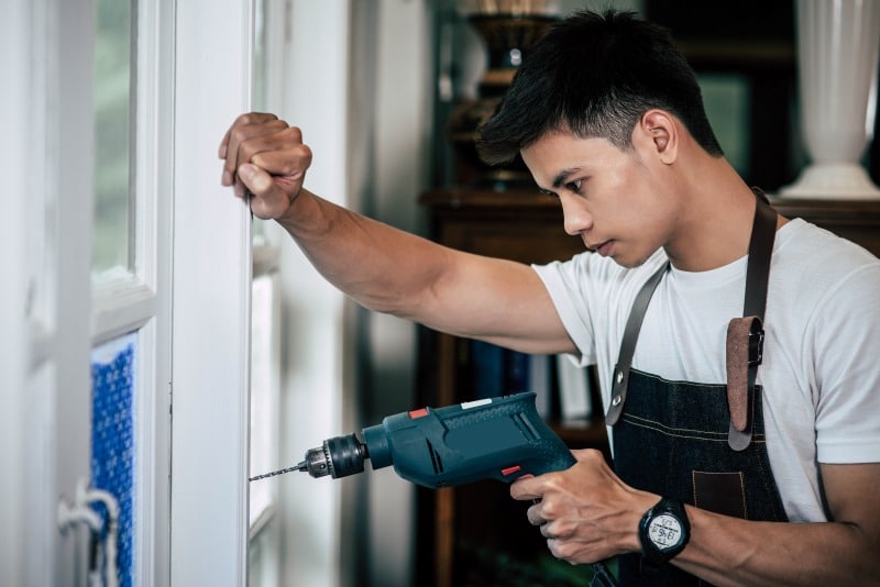 7 Signs Your Home’s Windows Need to Be Replaced Contractor using a power drill while working on home windows.