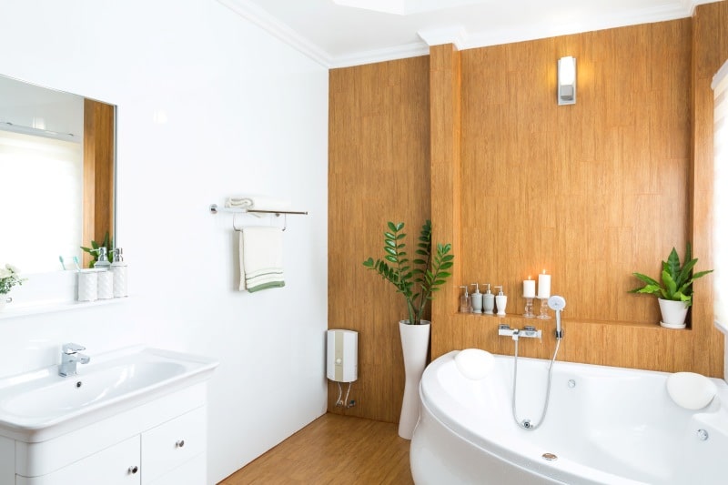 A Practical Guide To Creating A Safer, Easier-To-Clean Bathroom Bright safer bathroom with bathtub, sink, wood wall panels, handheld showerhead, and easy-to-clean surfaces.
