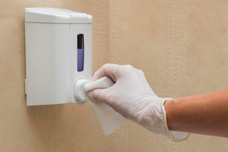 Hands-Free Hygiene: Finding the Best Dryer for Public Washrooms Gloved hand cleaning a wall-mounted hand dryer to maintain hygiene in a public washroom.