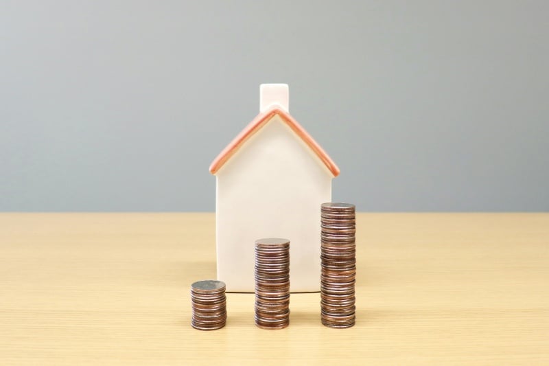What a Typical Home Sale Actually Looks Like From Start to Finish House model with stacked coins representing home sale costs and seller proceeds.