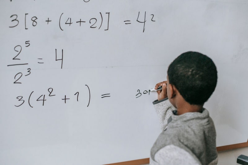 Building STEM Confidence Early: What Parents and Teachers Can Do Child solving math problems on a whiteboard while building STEM confidence through hands-on learning.