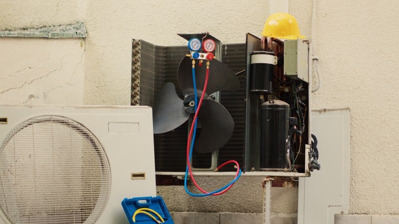 The Ultimate Checklist for an AC Not Cooling Properly HVAC technician inspecting an outdoor AC unit with exposed compressor, cooling fan, and pressure gauges to diagnose AC not cooling properly.
