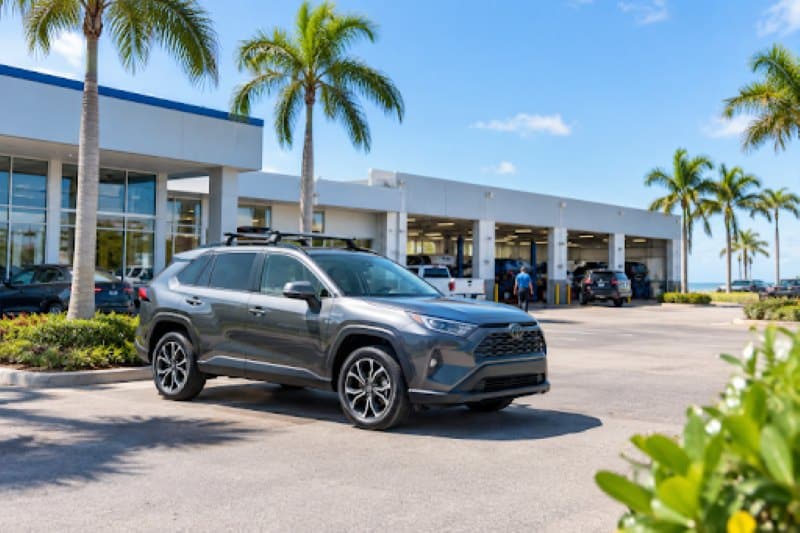 Car Parts Buying Checklist: Fitment, Safety, Cost & Installation Gray SUV parked outside an auto dealership and service center with palm trees, highlighting car parts and maintenance services.