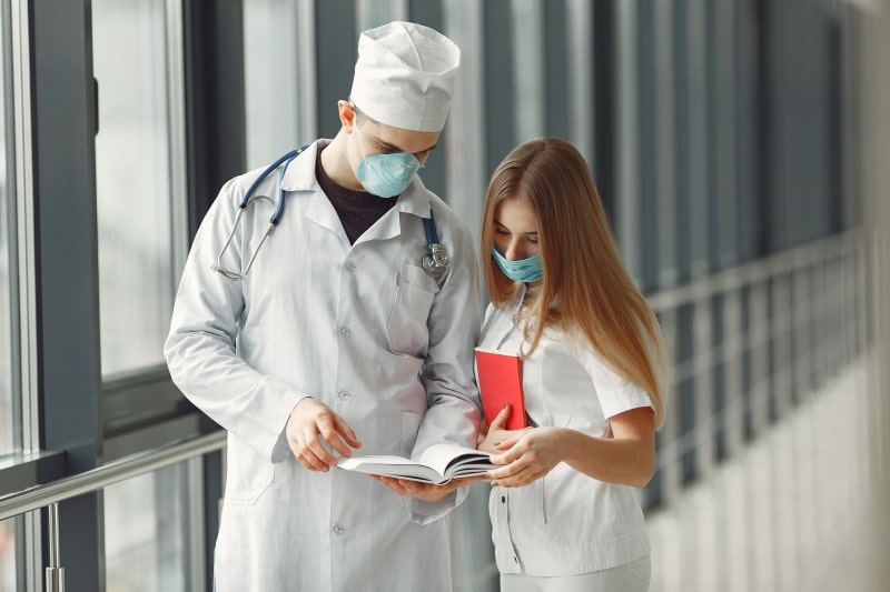 What Healthcare Providers Can Learn From the Hospitality Industry Two healthcare professionals wearing medical masks review a document together in a hospital corridor, highlighting communication in healthcare