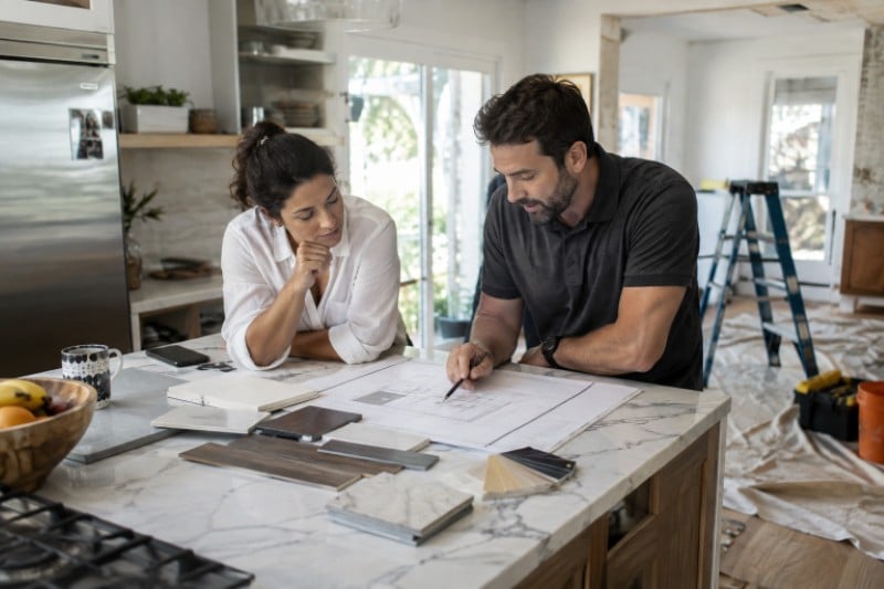 5 Best Miami Home Design-Build And Remodeling Firms Two people reviewing Miami home remodeling plans and material samples at a kitchen island.