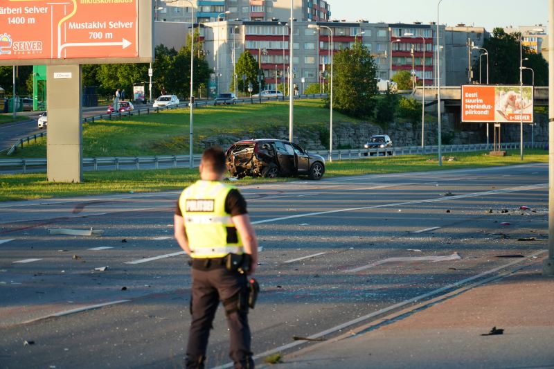 Police officer standing at a crash scene with a damaged vehicle and debris scattered across the roadway.