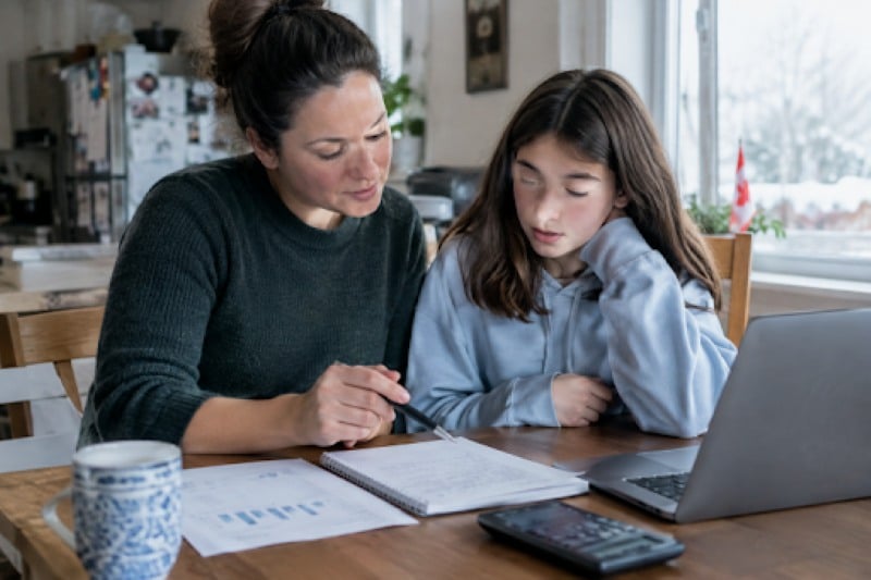 Mother and daughter reviewing financial paperwork and savings plans together at a kitchen table.